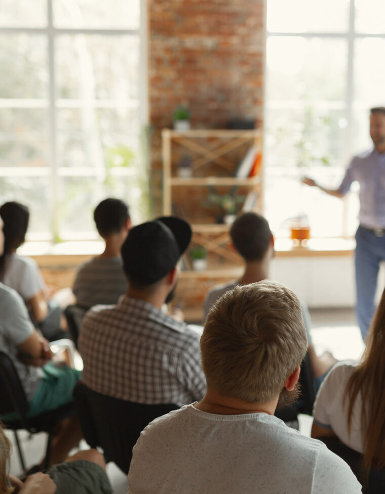 Male speaker giving presentation in hall at university workshop. Audience or conference hall. Rear view of unrecognized participants in audience. Scientific conference event, training. Education concept.